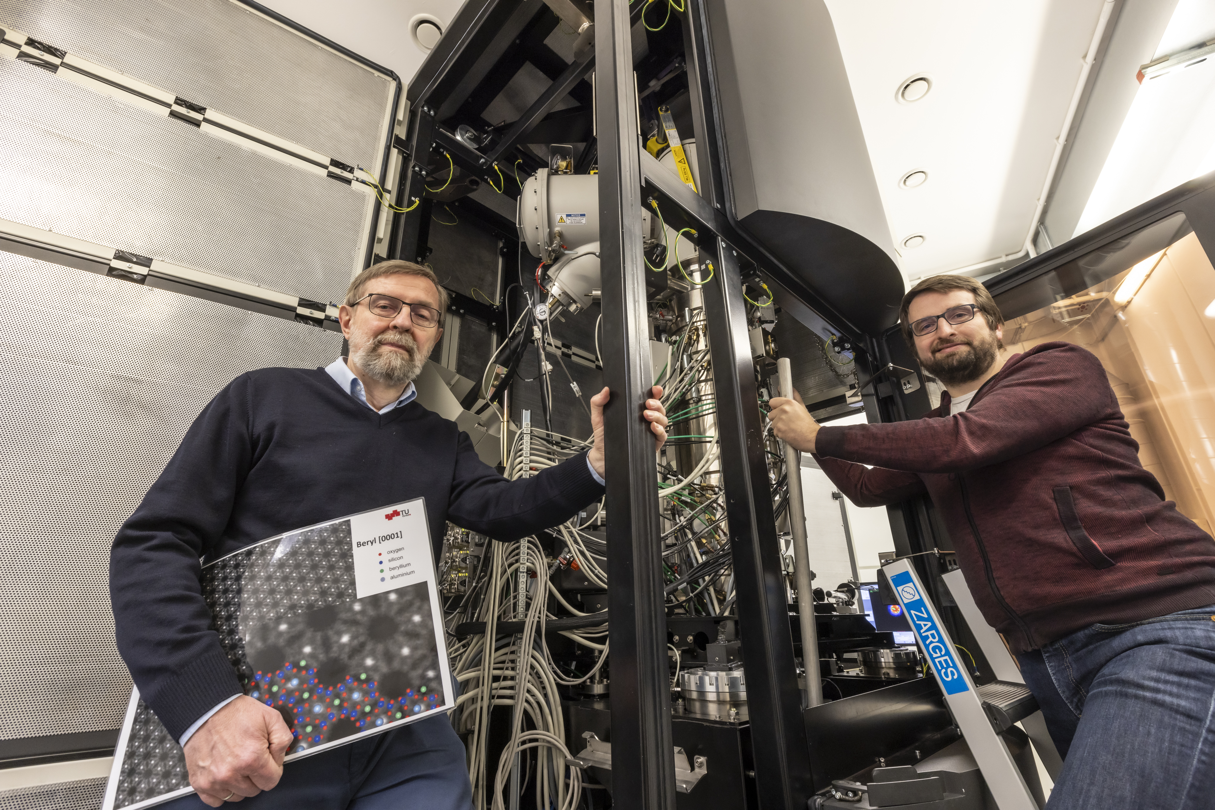 Zwei Männer stehen neben einer Maschine, in deren Inneren viele Kabel zu sehen sind.